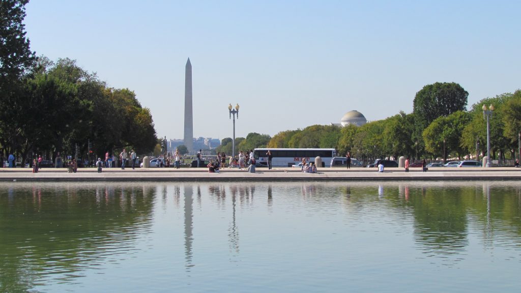 Bus passing by National Mall, Washington Monument with bustling crowds of people enjoying the attractions.